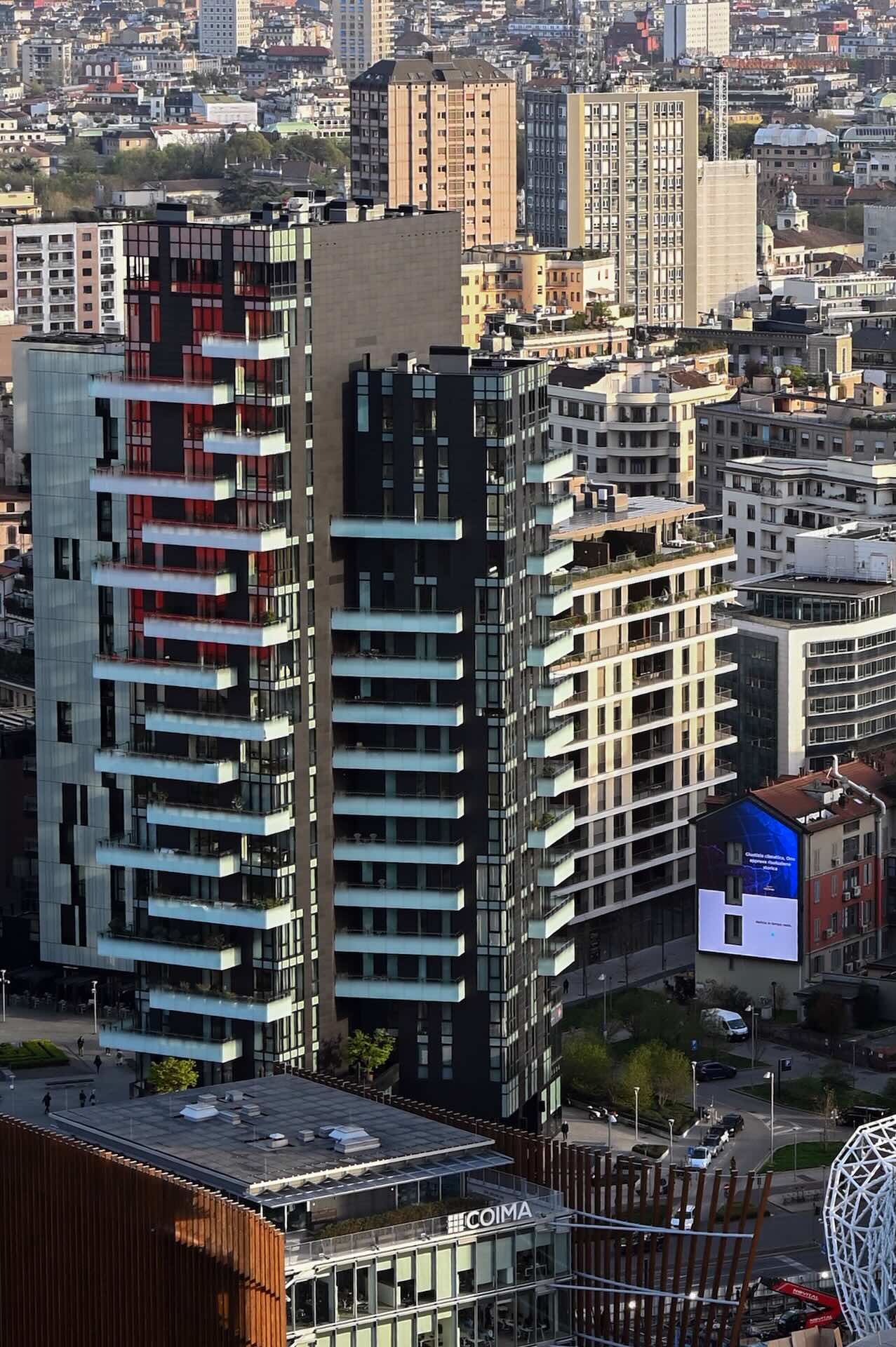 Vista aerea diurna della Torre Solea accanto alla torre residenziale con facciata rossa, con l'insegna COIMA a livello strada.