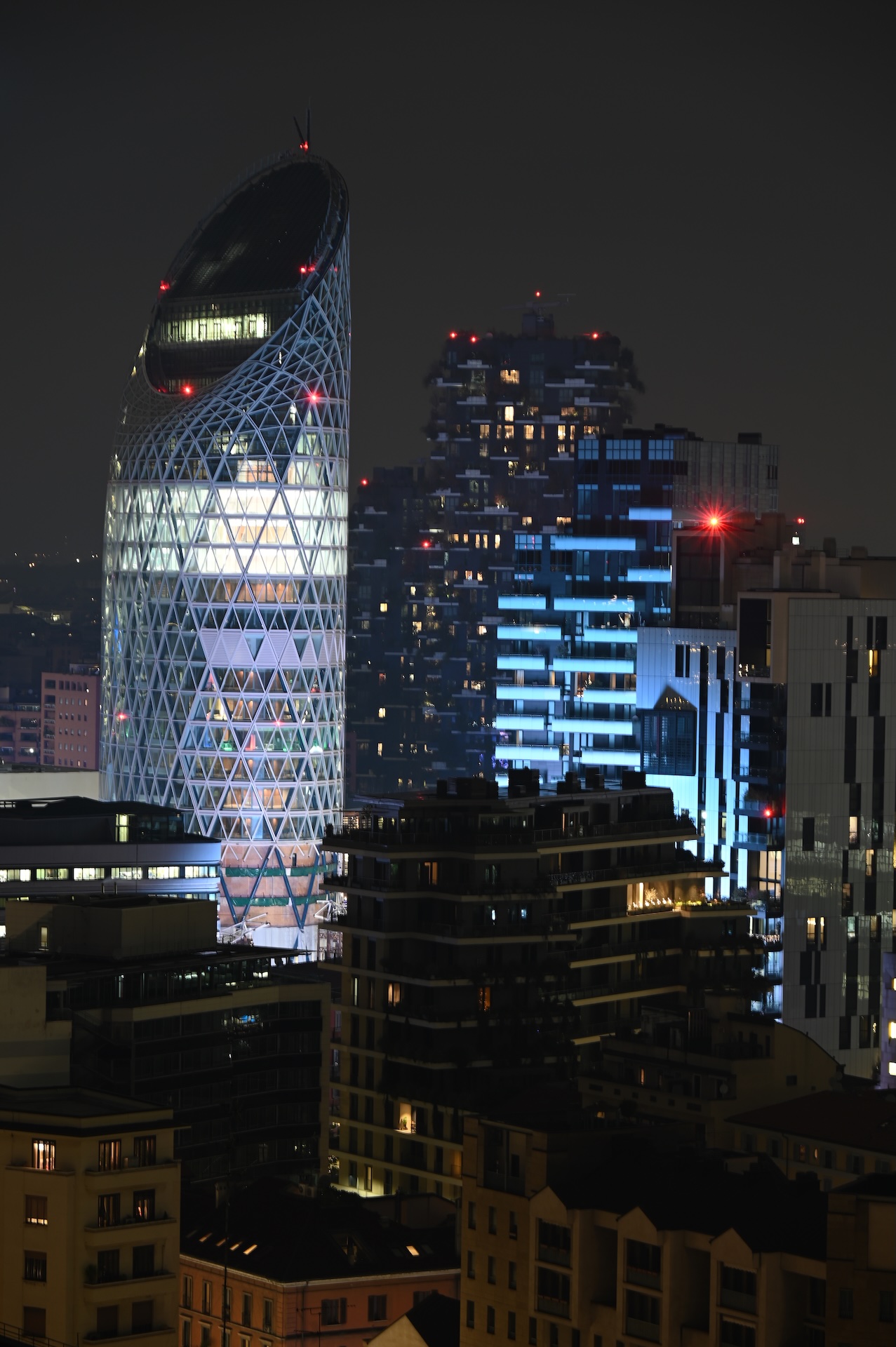 La Torre Unipol illuminata di notte, ancora in costruzione, accanto al Bosco Verticale.